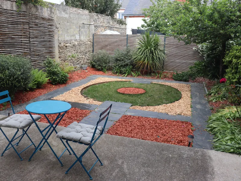 Table et chaises de jardin sur la terrasse ombragée, ouverte sur le jardin partagé